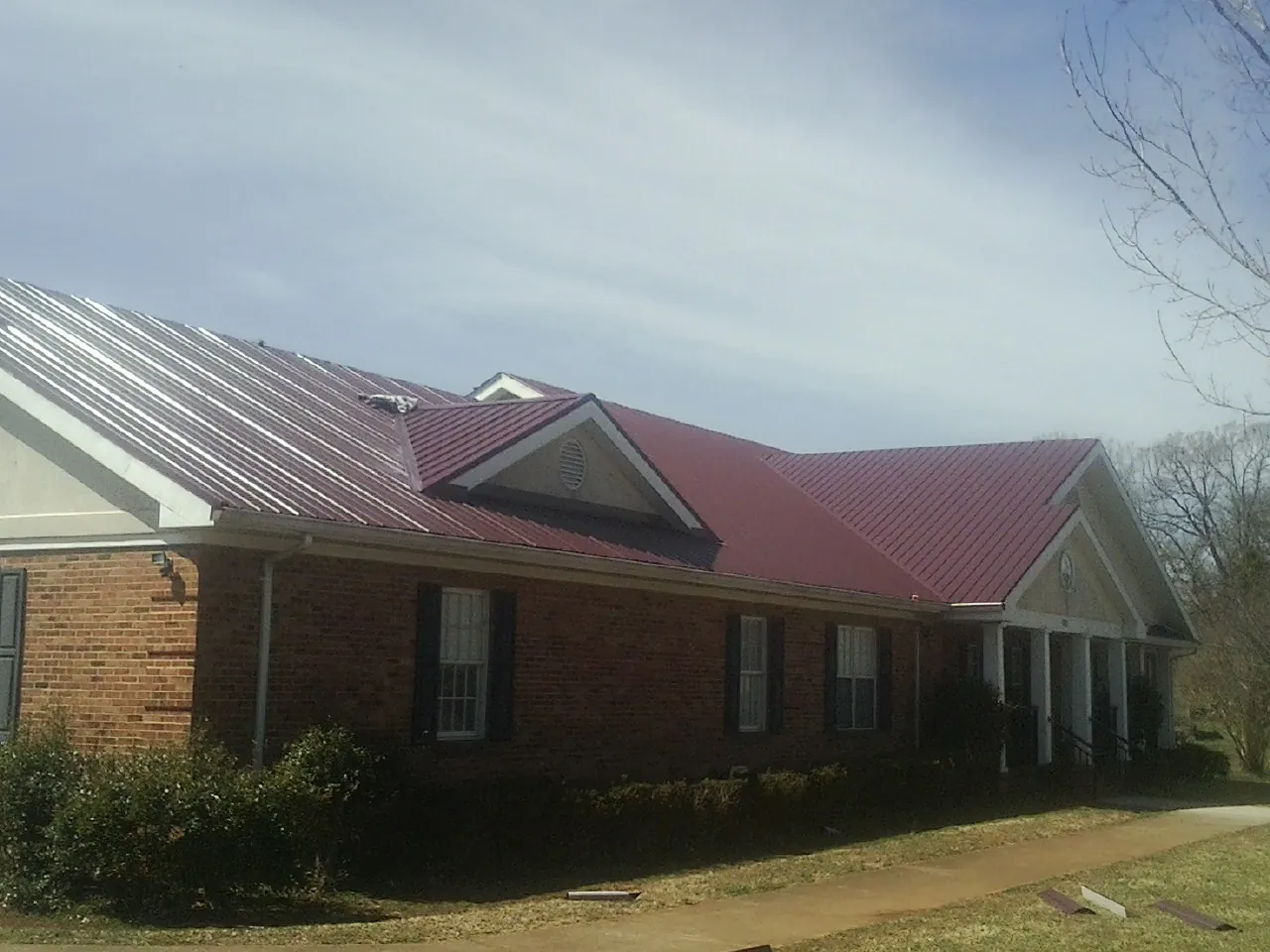 Red metal roof with gabled entries on a long brick building, from a Hail Damage Roof Repair job in Drifton