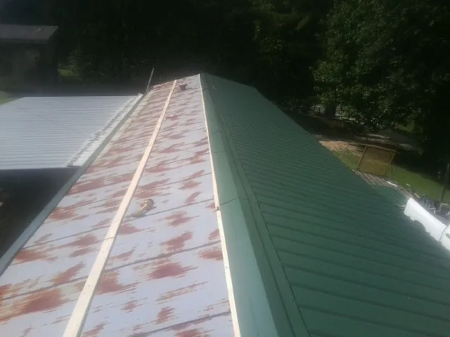 Old rusted panels beside newly installed green metal roofing — Wind Damage Roof Repair by Roofing Brothers in Drifton