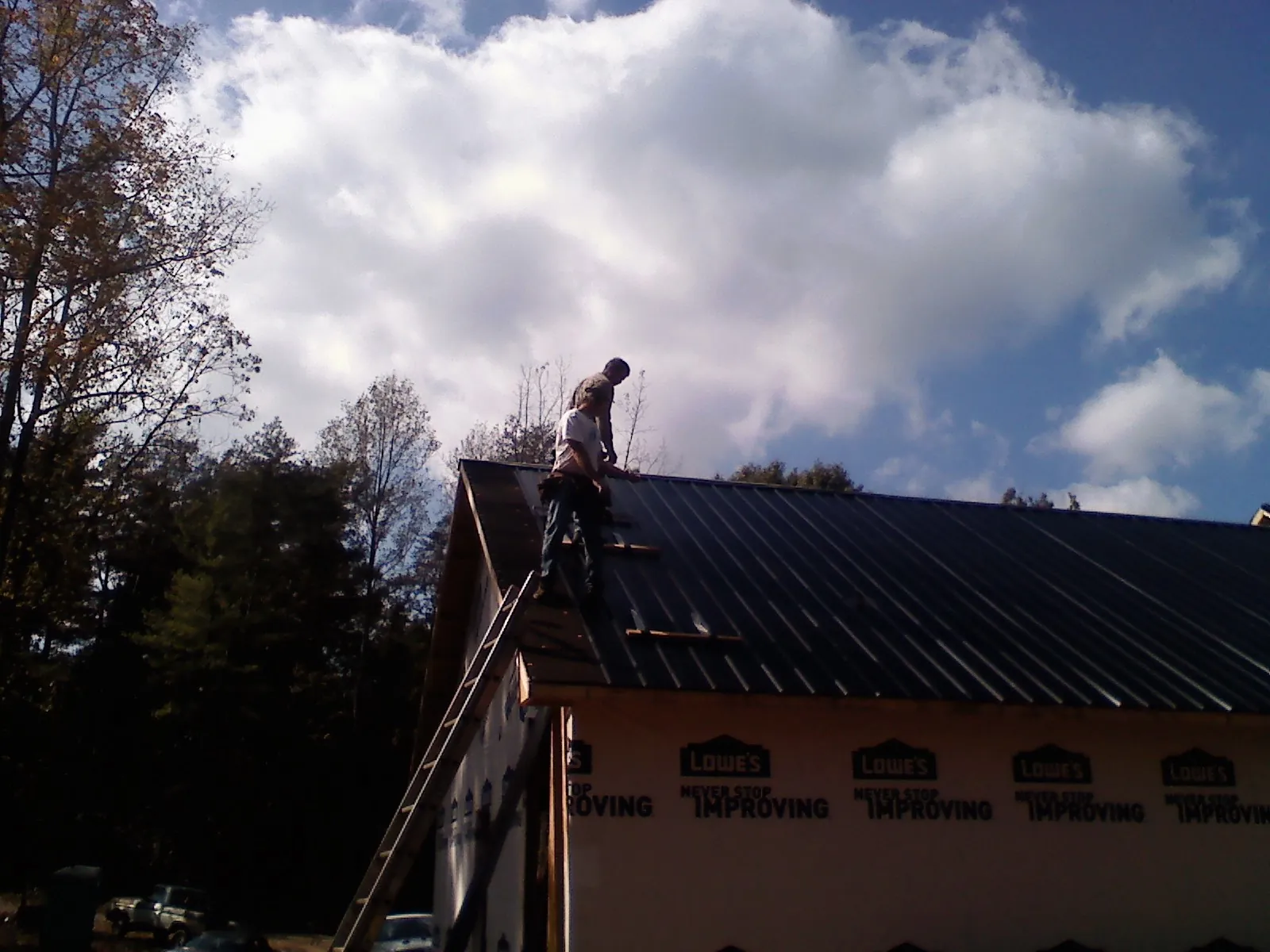 Roofer fastening dark metal panels high against a cloudy sky, from a Roof Inspection job in Drifton