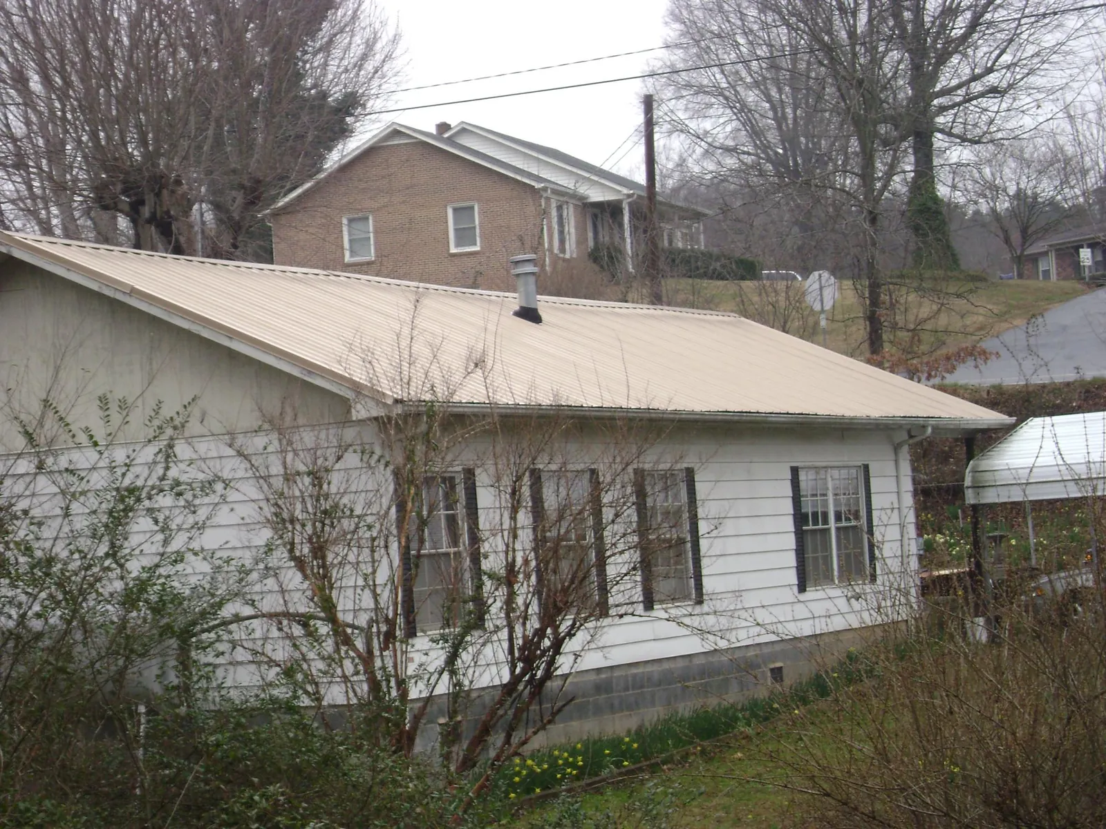 Tan metal roof on a white sided house set into a hillside — Commercial Roofing by Roofing Brothers in Drifton